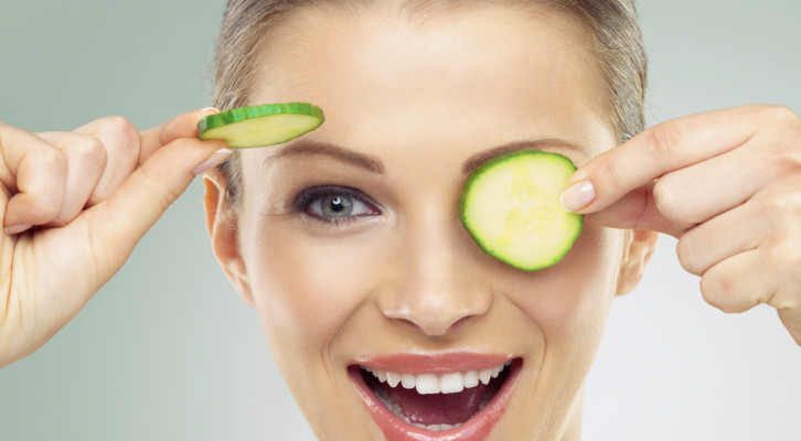 Studio portrait of a beautiful young woman posing with two cucumber slices against a green background